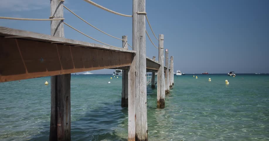 A wooden pier with rope railings stretches across clear turquoise water under a bright blue sky