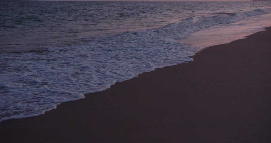 Gentle waves roll onto a dark sandy beach at dusk