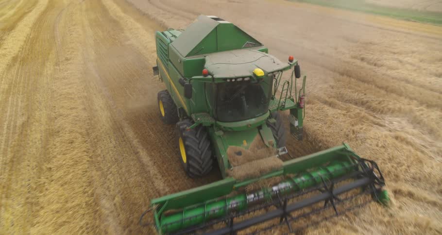 An aerial view captures a green combine harvester cutting through a vast golden wheat field
