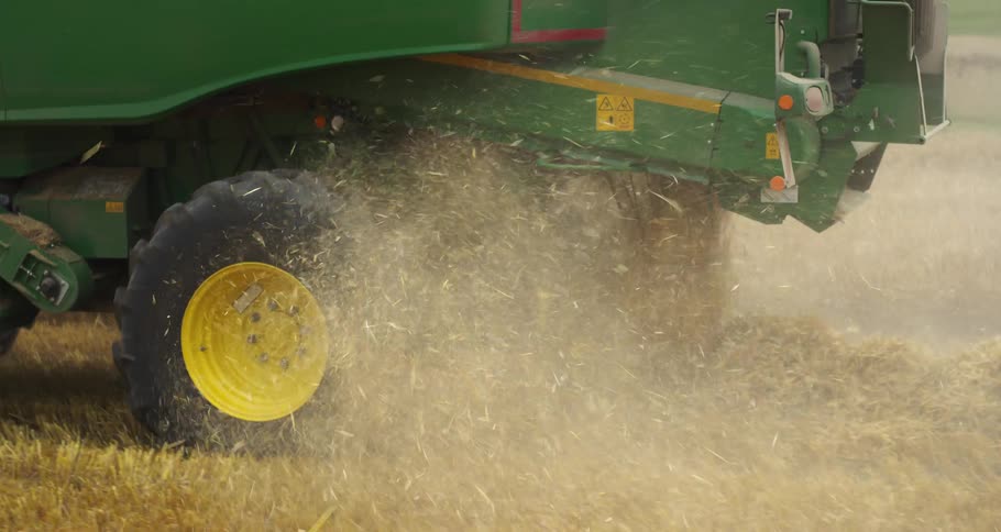 Agricultural harvester wheel kicking up dust and straw during harvesting