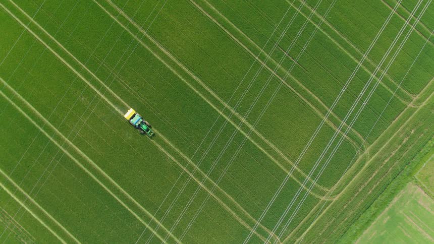 An aerial view captures a tractor working in a vast vibrant green field crisscrossed by power lines