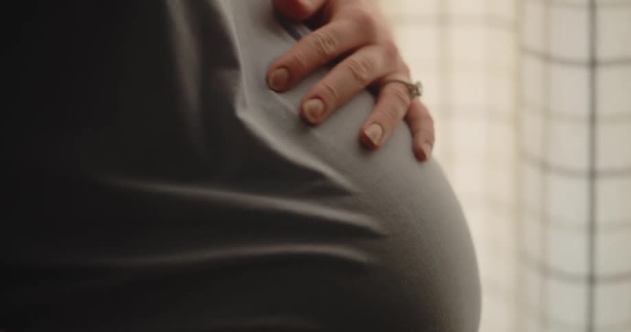 Adult pregnant woman touching her belly with her hand indoors