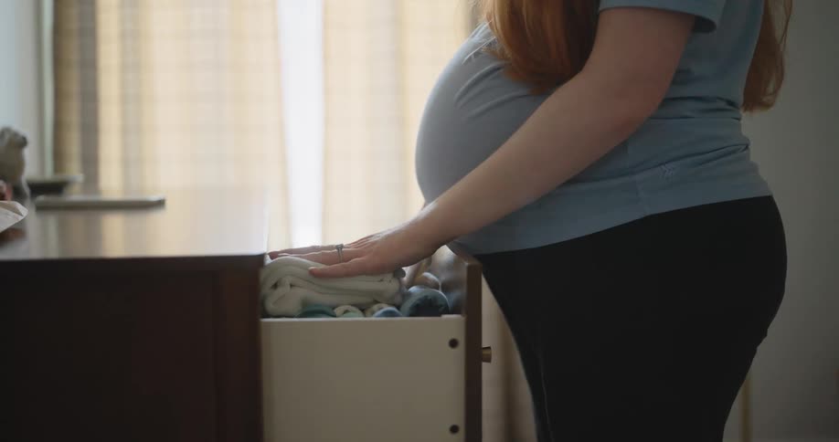The pregnant woman is putting away clothes