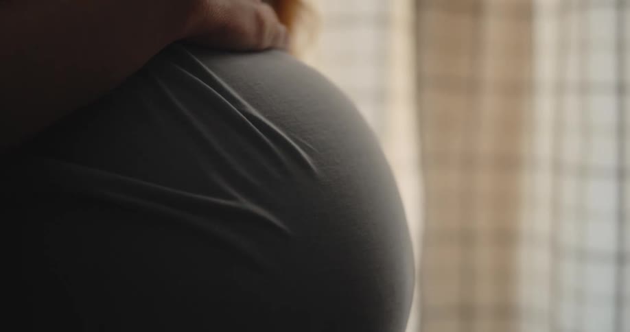 Hands resting on a pregnant belly indoors