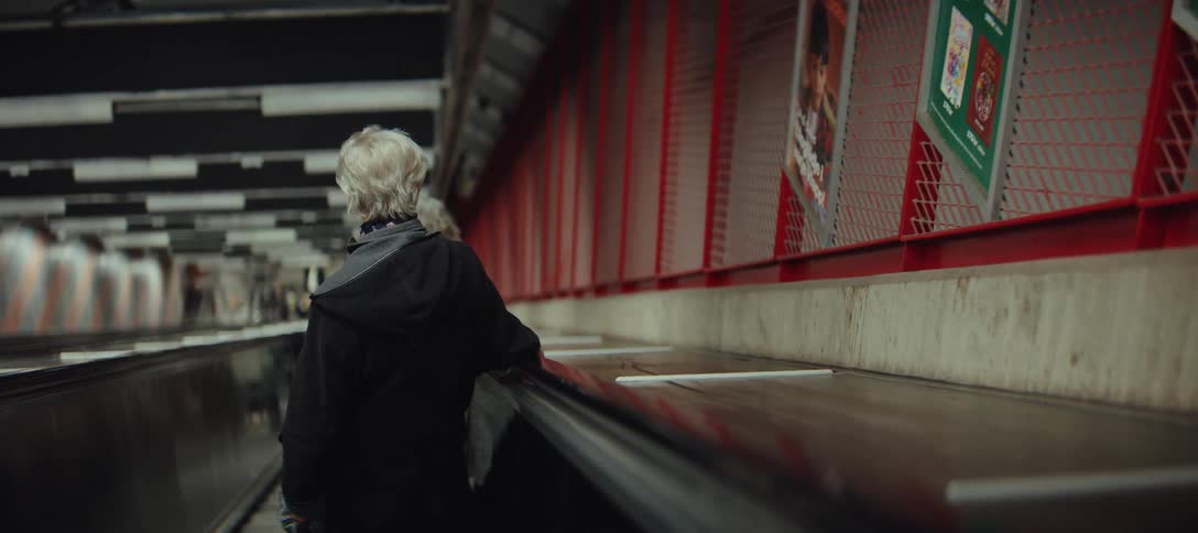 Person seen from behind on an escalator in a station with metal structure and artificial lighting around