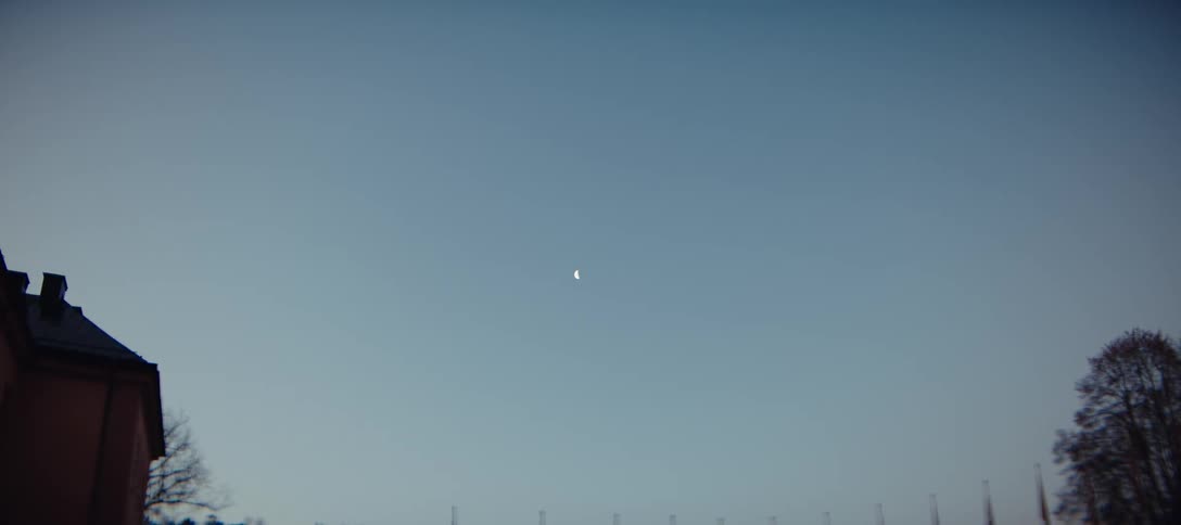 A crescent moon hangs in a clear blue sky during the evening