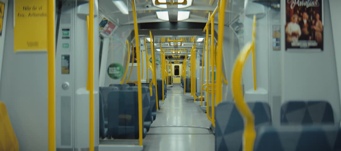 Empty train car interior with blue seats and yellow handrails aligned along the central aisle
