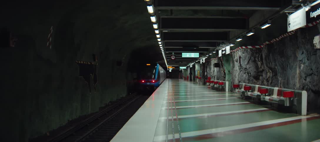 A blue subway train pulls away from an empty platform and enters a dark tunnel