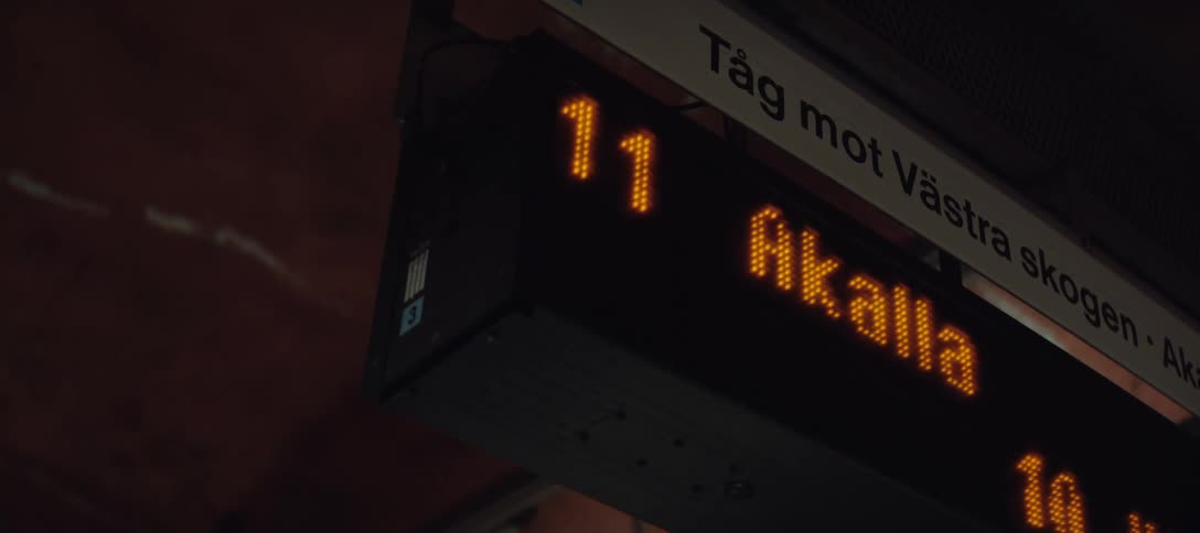 A digital sign in a terminal displays time and travel information glowing above the busy walkway