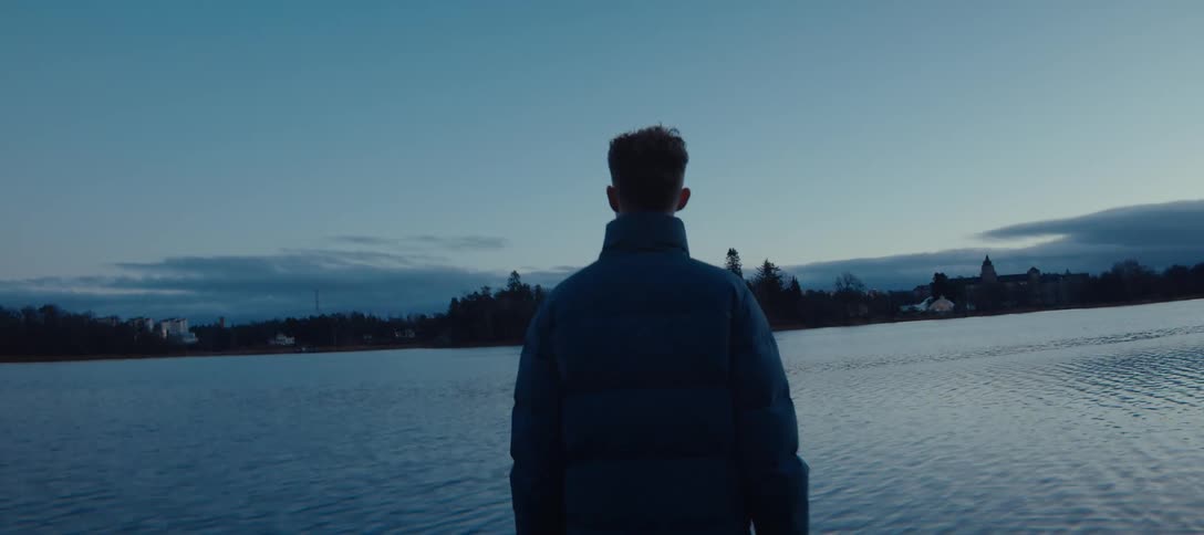 A man is standing on the coast looking across the water at a city