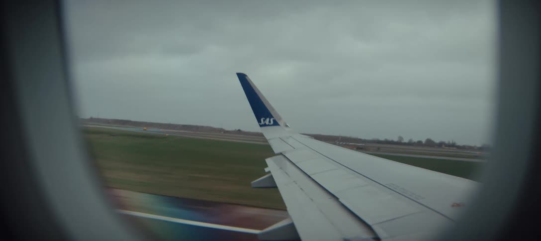 Airplane wing visible through the window during takeoff on a runway under cloudy skies