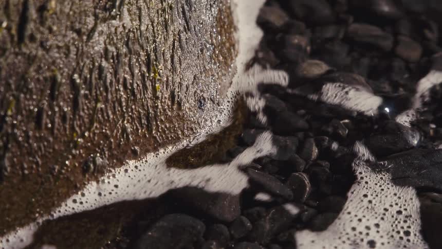 Wet rock with vertical grooves surrounded by dark pebbles