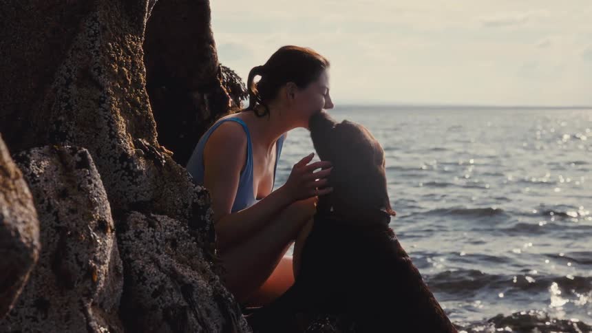 Woman sitting among seaside rocks petting a dog