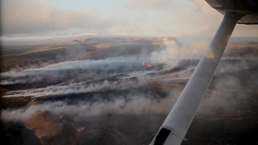 Aerial view of volcanic landscape with lava flow and smoke observed from a light aircraft