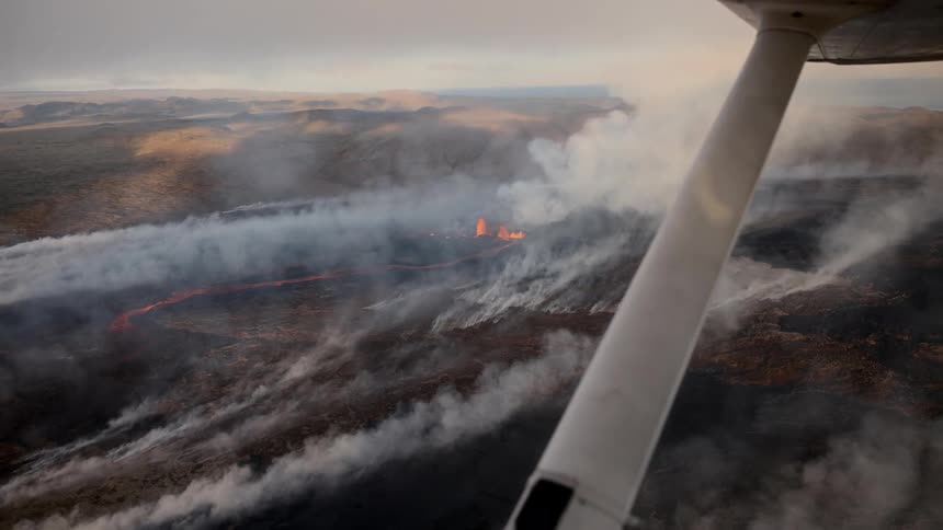 View from below of an airplane in full flight with an area on fire and smoke