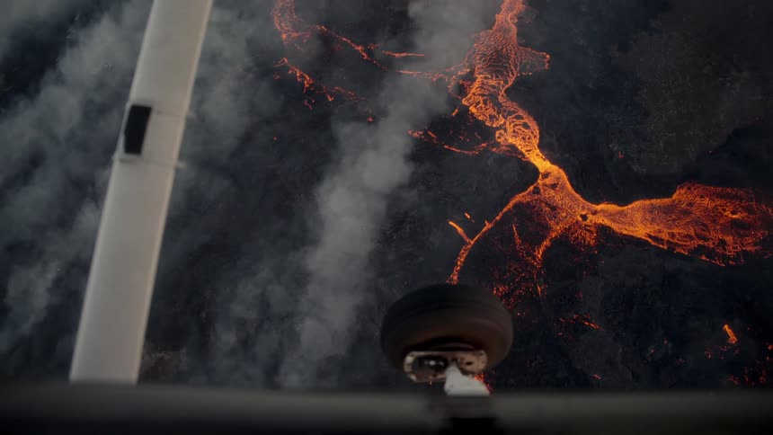 Incandescent lava snakes across dark terrain beneath rising steam aerial view reveals geological force