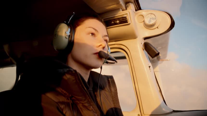 Pilot with headset watches goldenlit sky during flight in light aircraft