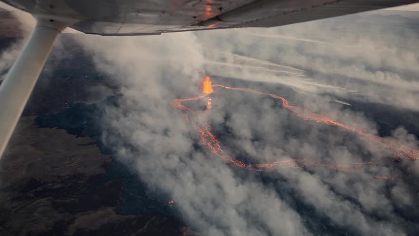 Glowing lava flows from active crater surrounded by volcanic smoke