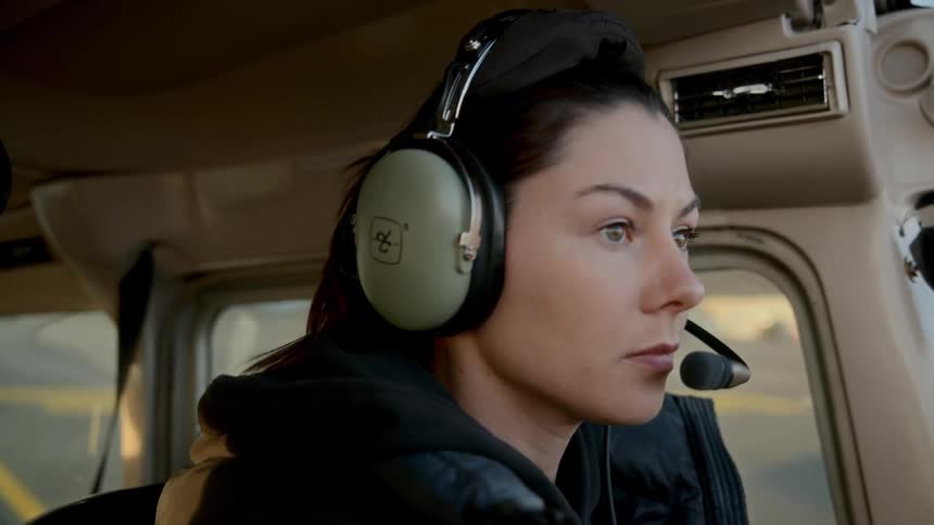 A woman sits in the cockpit of a small aircraft wearing professional aviation headphones with a builtin microphone
