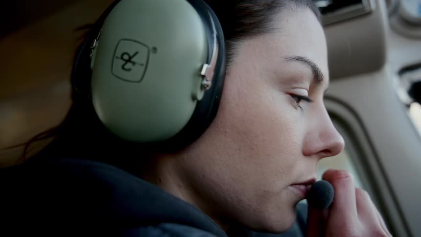 Person with headset and microphone focused inside aircraft cockpit with part of interior visible