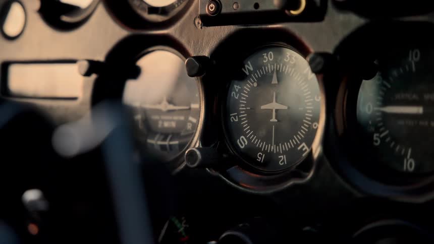 A closeup of vintage aircraft cockpit instruments focusing on a heading indicator and vertical speed gaugethe camera slowly pans across the dashboard as warm golden light reflects off the glass faces of the analog dials
