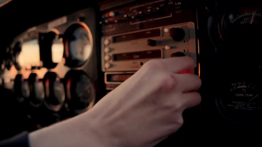 A persons hand is shown reaching out to adjust the knobs on an aircrafts radio and navigation stack within a dimly lit cockpitthe instrument panel surrounding the avionics includes various analog gauges such as an egt indicator and carburetor tempe