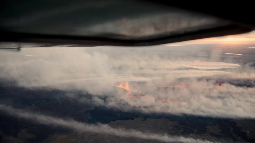 Incandescent lava spreads across dark landscape as thick smoke rises aerial view reveals eruptions force