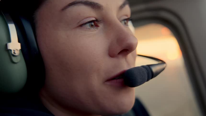 Person wearing headset and microphone facing forward in aircraft cockpit during sunset