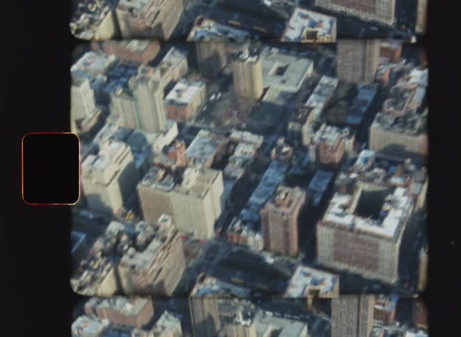 An aerial perspective looking down at a dense cluster of city apartment buildings and skyscrapers the camera moves slowly revealing the varying heights rooftop textures and the geometric grid of the urban landscape below