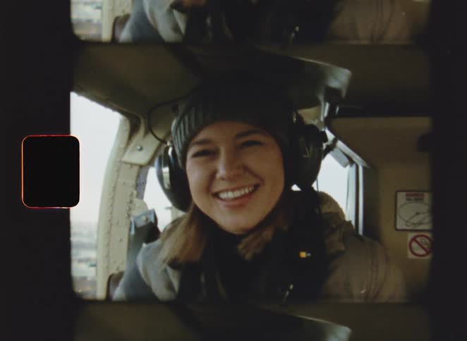 A woman wearing a headset smiles at the camera inside an aircraft