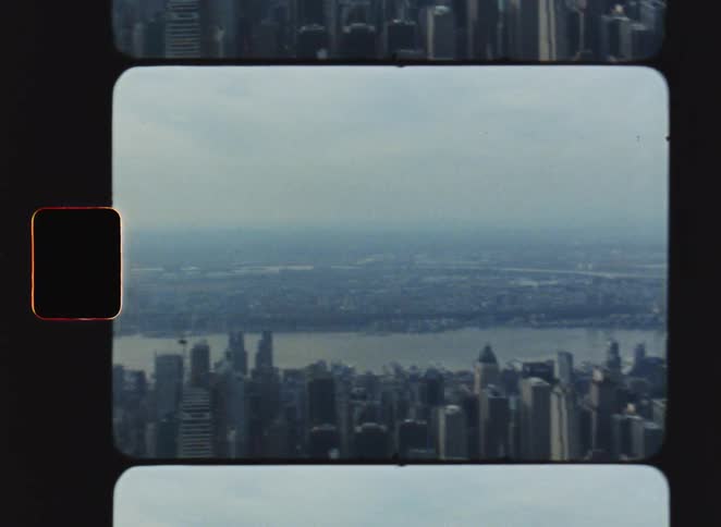 A vintage film style aerial view shows the new york city skyline with many skyscrapers and a wide river under a hazy sky