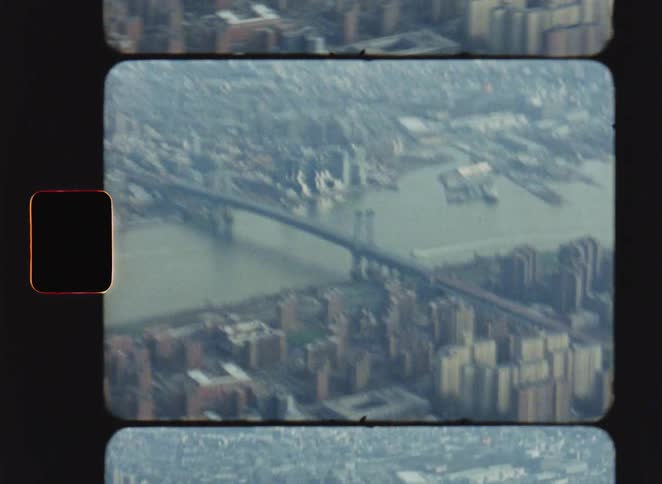 This video features a grainy vintagestyle aerial shot of a suspension bridge spanning a wide river in a dense urban environment the footage is framed with a nostalgic film reel aesthetic complete with visible sprocket holes and a muted color palette
