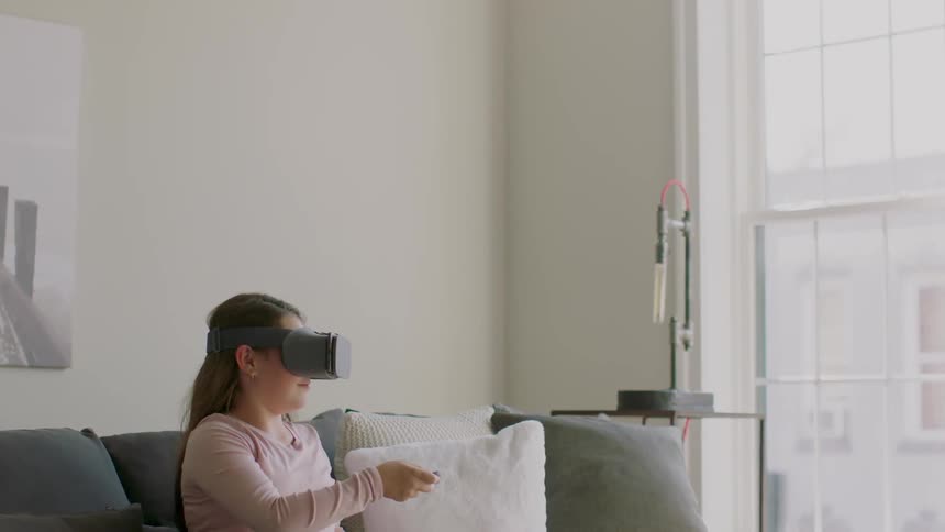 Little girl sitting on couch wearing virtual reality headset and playing game