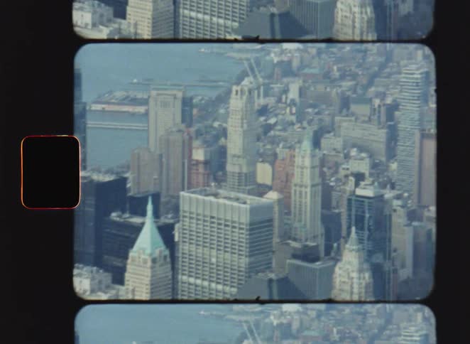 A view from above shows many tall buildings in a city and a body of water in the distance