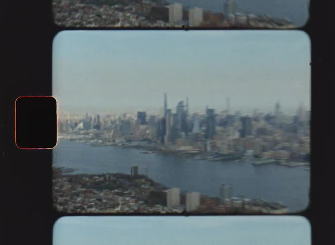 A vintage film style aerial view shows the new york city skyline with many skyscrapers and a wide river under a hazy sky