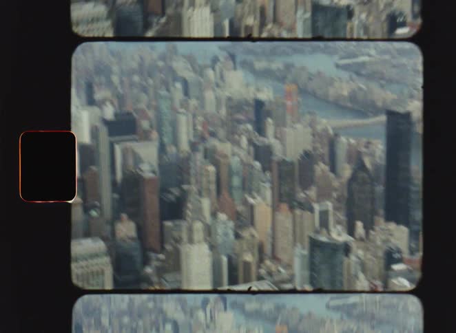 Vintage film footage shows a high view of a dense city skyline with numerous skyscrapers and office buildings under a soft daylight sky with a river visible in the distance
