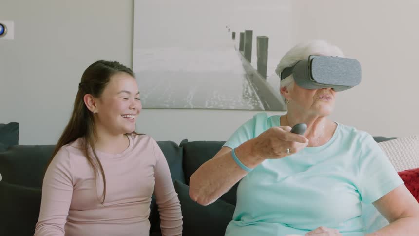A girl laughs as an older woman uses virtual reality