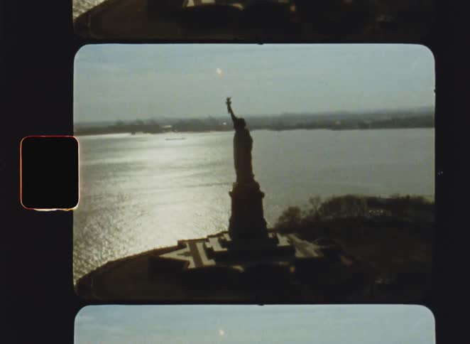 Statue of liberty seen from behind facing a body of water at dusk