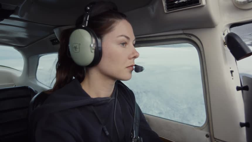Woman with headset facing forward in aircraft cockpit flying over snowcovered region