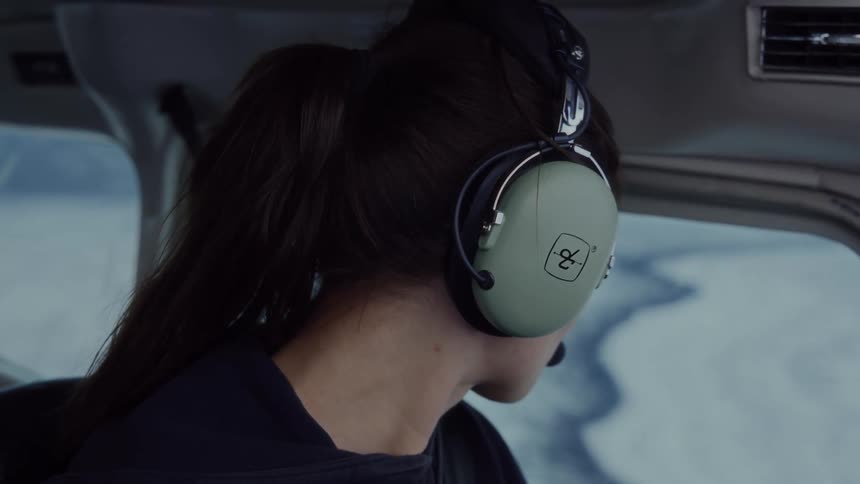 Person with headset observing snowy landscape through aircraft window during flight over remote region