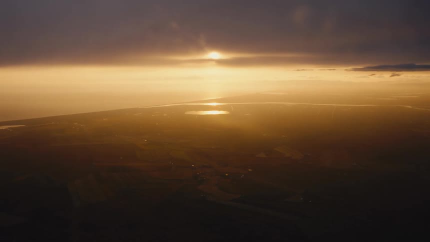 Sun obscured by clouds over fields and lake at dawn