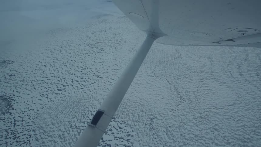 An aircraft flies over a frozen arctic sea at midday spinning slightly as it moves along a white path of ice below
