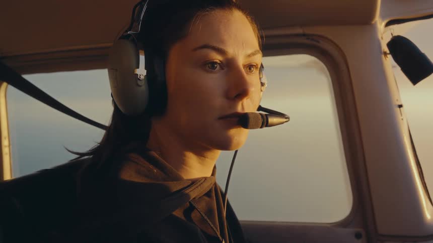 Woman with headset observing golden sky through aircraft window during flight