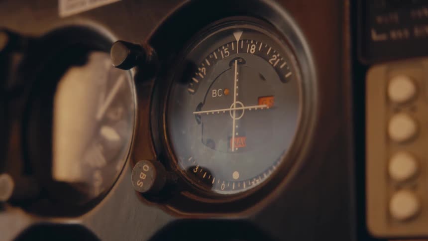 A close view shows the illuminated dials and gauges on the control panel inside an airplane cockpit as the needles move during flight