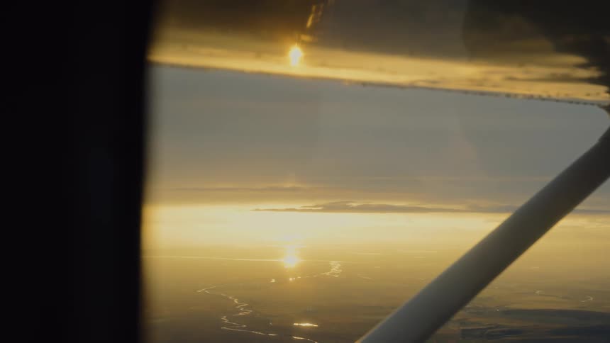 Aerial view of sunset through an aircraft window with sun reflection and rivers below
