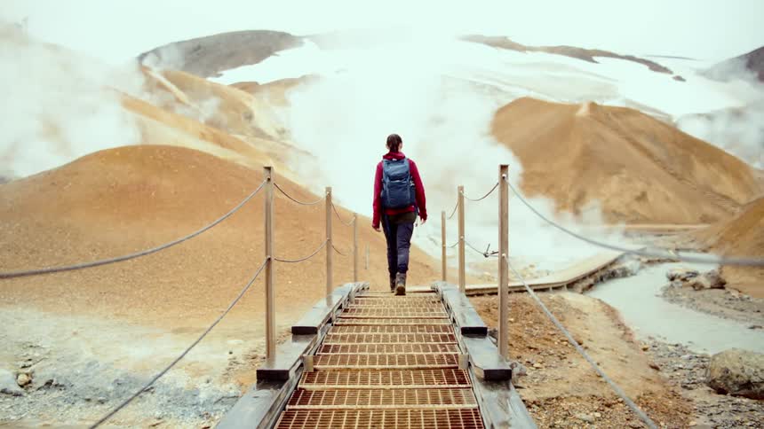 The woman walks towards the geysers on the mountain