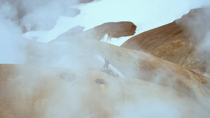 Person walking across geothermal terrain with steam and rock formations