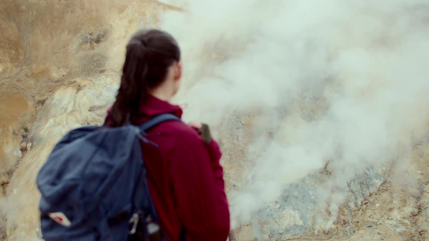 Woman in red jacket and backpack amidst volcanic mountains