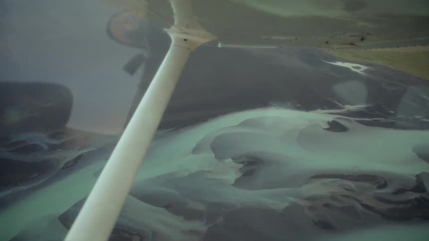 A view from a small airplane shows winding turquoise rivers and dark sand bars flowing through a vast landscape