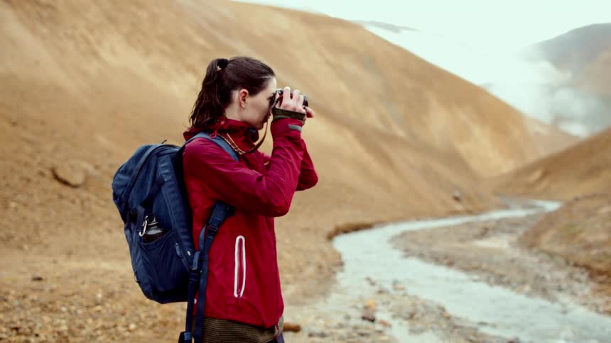 The woman is taking pictures by the mountains
